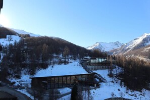 Un bâtiment moderne à la façade vitrée, situé dans une région montagneuse enneigée, sous un ciel dégagé.