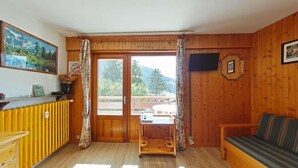 Ein Zimmer mit Holzboden, einer Couch, einem Tisch und einem Fenster mit Vorhängen.