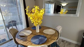 Un coin repas avec une table ronde, des chaises, un vase rempli de fleurs jaunes et un miroir au mur.
