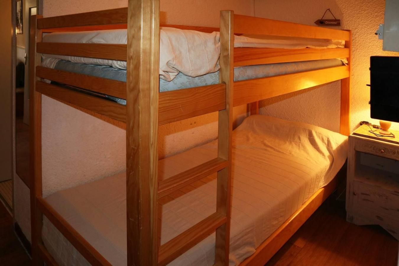 Een stapelbed met houten frame, een nachtkastje met lamp en een wandplank.