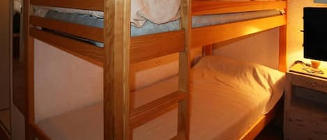 A bunk bed with a wooden frame, a bedside table with a lamp, and a wall-mounted shelf.
