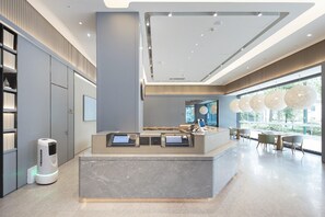 A modern reception area with a marble counter, digital kiosks, and a view of the outdoors through large windows. - Ji Hotel (Changzhou)