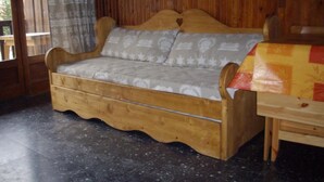 Een houten bank met een kussen met een patroon in een kamer met houten wanden en een betegelde vloer.