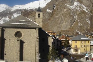 A historic stone building with a bell tower, surrounded by snow-covered mountains and modern buildings.
