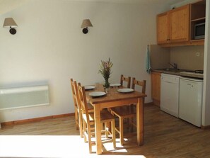 A dining area with a wooden table and chairs, a vase with flowers, and a kitchen with wooden cabinets and a microwave. - Ski-in/ski-out & foot of the slopes, view ski slopes, swimming pool, sauna, balcony, tv, 36m² (Les Orres)