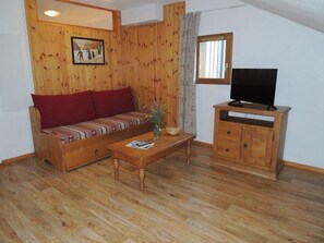 Ein Wohnzimmer mit Holzboden, einer Couch, einem Fernseher auf einer Holzkommode und einem gerahmten Bild an der Wand.