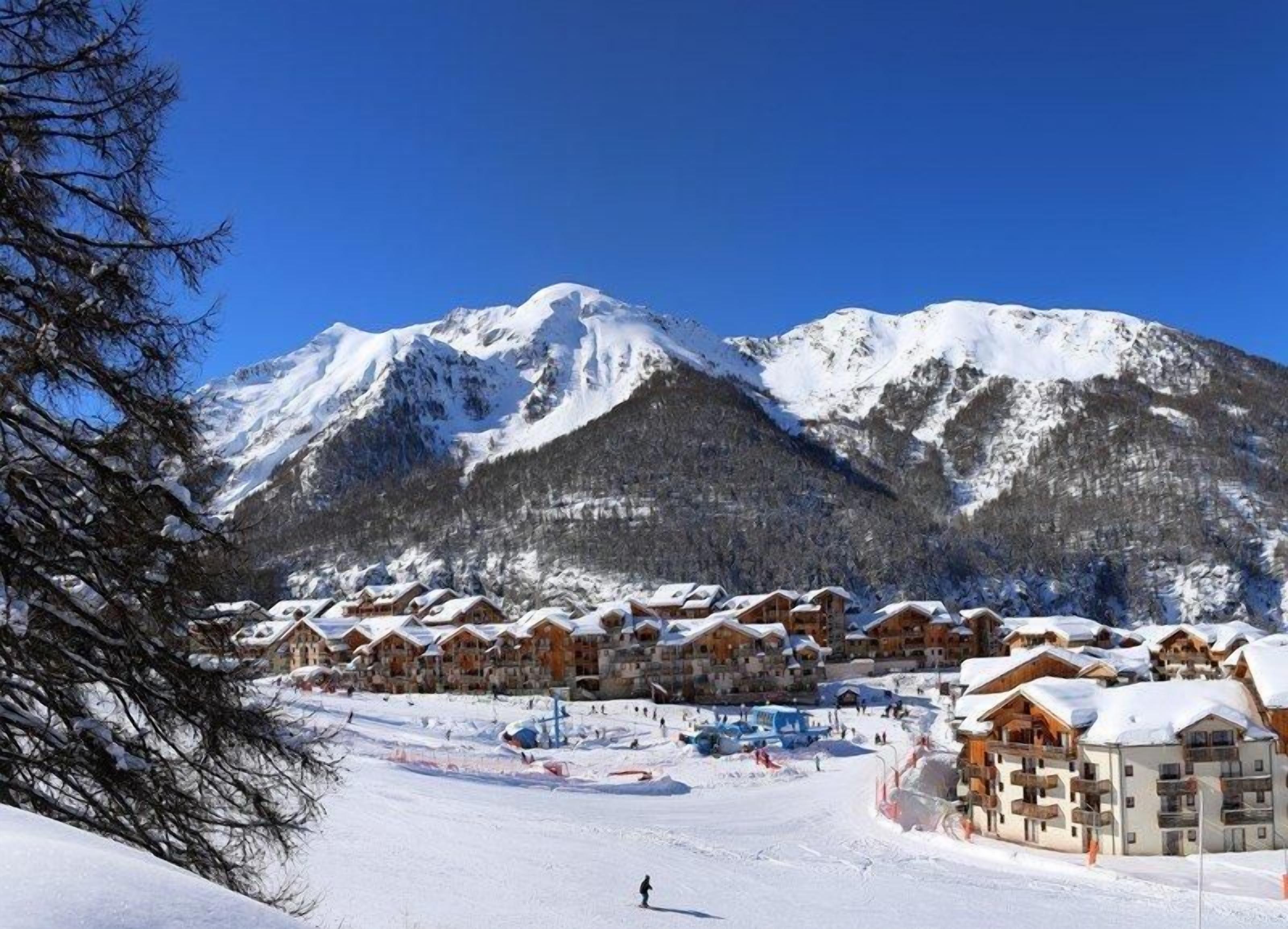 A snow-covered mountain resort with wooden chalets and a ski slope.