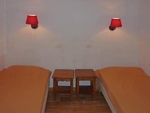 A room with two single beds, a small wooden table, and two wall-mounted lamps.