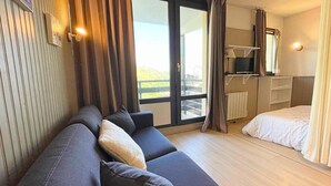 A modern hotel room with a sofa, a bed, a balcony with curtains, and a view of the outdoors. - 10m from ski slopes, 2nd floor, view mountain, balcony, tv, ski locker, 26m², Les Menuires (Les Menuires)