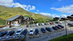 A parking lot with multiple cars and a building with balconies, set against a mountainous backdrop. - 10m from ski slopes, 2nd floor, view mountain, balcony, tv, ski locker, 26m², Les Menuires (Les Menuires)