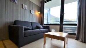 A modern living room with a dark grey sofa, a wooden coffee table, and a large window offering a view of a mountainous landscape. - 10m from ski slopes, 2nd floor, view mountain, balcony, tv, ski locker, 26m², Les Menuires (Les Menuires)