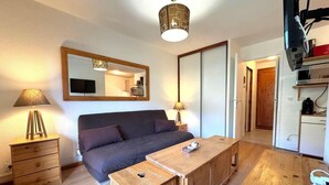 A cozy room with a bed, a wooden table, a lamp, and a mirror. - 10m from ski slopes, 1st floor, view ski slopes, balcony, tv, ski locker, 30m², Les Menuires (Les Menuires)