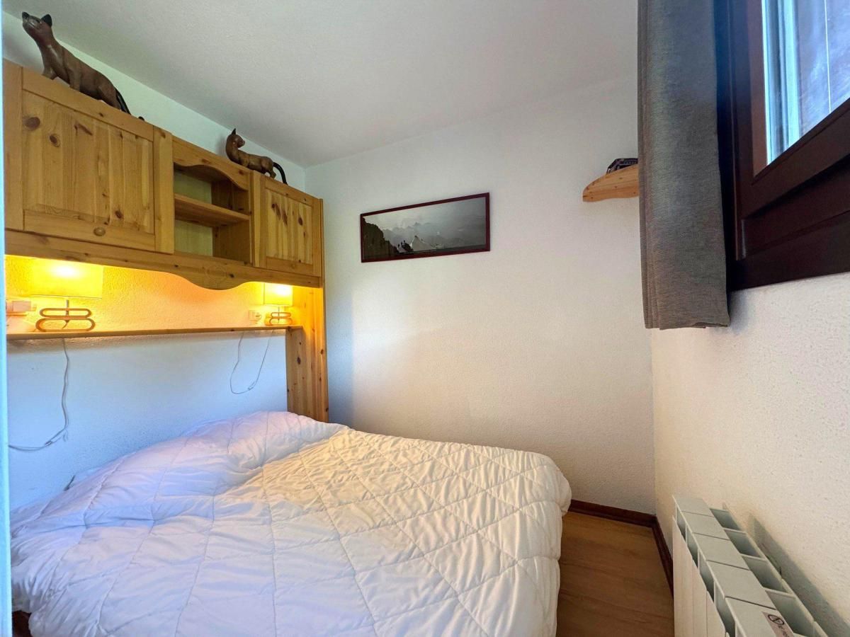 Un dormitorio pequeño con cama, cabecera de madera, estante de pared con figuritas, un cuadro enmarcado y una ventana.