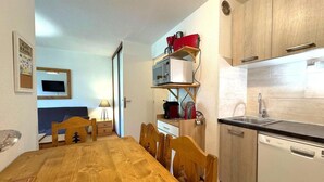 A compact kitchen with a wooden table and chairs, a microwave, a coffee maker, and a dishwasher. - 10m from ski slopes, 1st floor, view ski slopes, balcony, tv, ski locker, 30m², Les Menuires (Les Menuires)