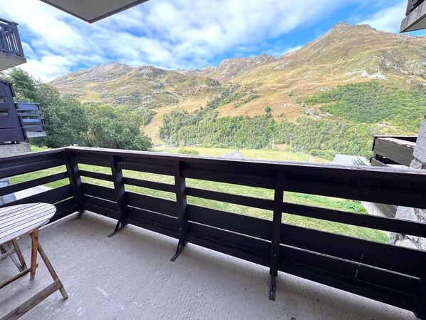 A balcony with a wooden table and chairs, overlooking a mountainous landscape.