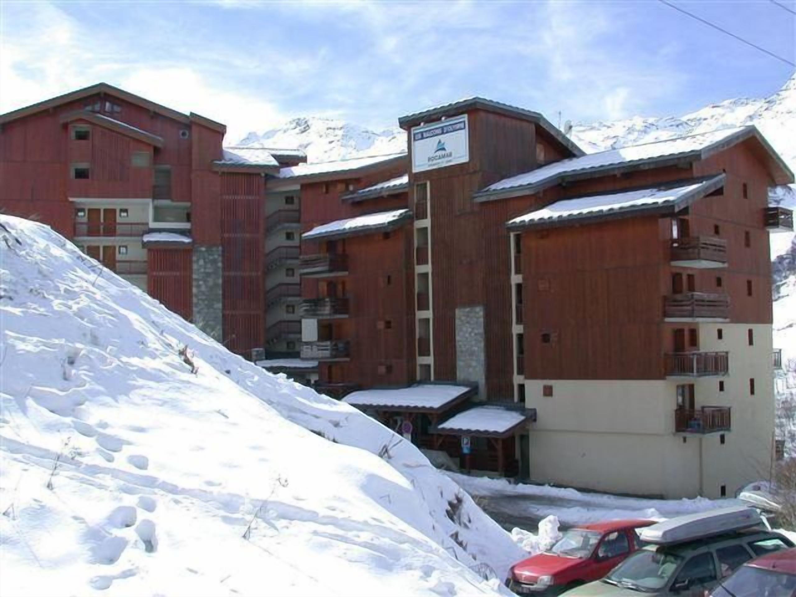 Un edificio de varios pisos con fachada de madera y balcones, rodeado de terreno cubierto de nieve.