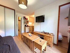 A compact room with a bed, a wooden desk, a television, and a kitchenette.