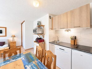 A compact kitchen with white cabinets, a built-in microwave, and a sink. There is a dining table with chairs and a small side table with a lamp. - 10m from ski slopes, 1st floor, view ski slopes, balcony, tv, ski locker, 30m², Les Menuires (Les Menuires)