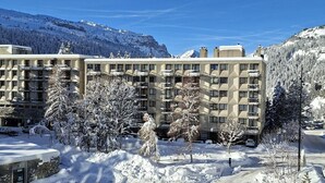 A multi-story hotel with a symmetrical facade, surrounded by snow-covered trees and mountains.
