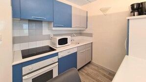 A compact kitchen with blue and white cabinetry, a microwave, a sink, and a stove.