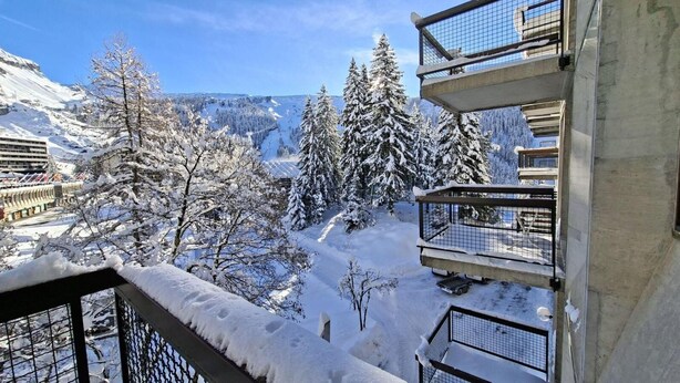 A snow-covered balcony with a view of a snowy mountain landscape and trees.