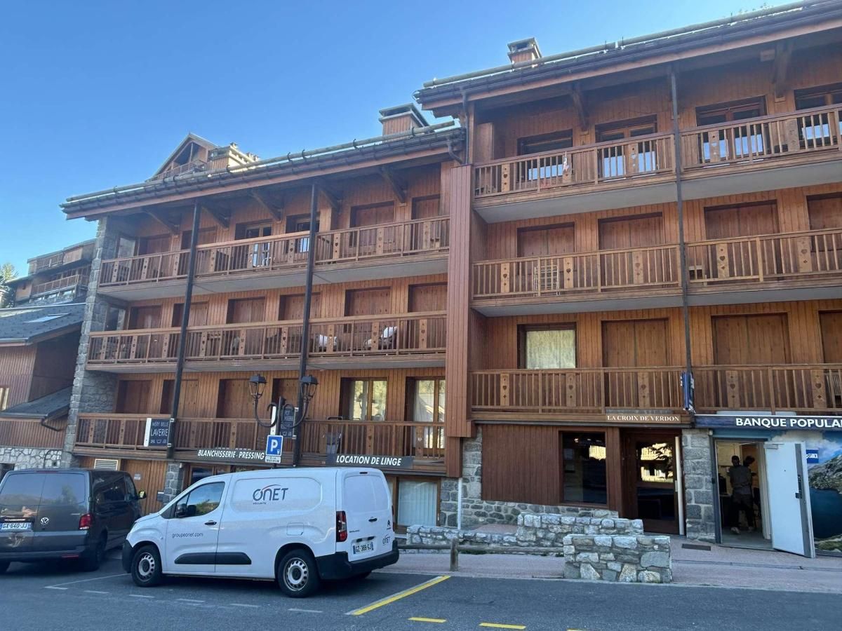 Un edificio in legno a più piani con balconi, un'area di parcheggio e negozi, tra cui una banca e una tipografia.
