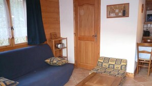 A cozy living area with a sofa, a wooden coffee table, a patterned armchair, and a wooden door. - 1st floor, view village, terrace, tv, ski locker, 39m², Méribel (Les Allues)