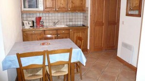 A compact kitchen with wooden cabinets, a tiled backsplash, a white microwave, and a small dining table with chairs. - 1st floor, view village, terrace, tv, ski locker, 39m², Méribel (Les Allues)