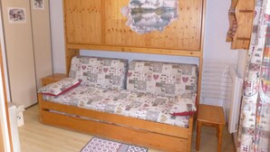 A wooden sofa with patterned cushions, a wooden headboard with a cut-out, and a small wooden table beside it.