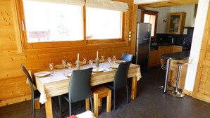 A wooden interior with a dining table set for four, a kitchen area with modern appliances, and a cozy seating area with a red cushion.