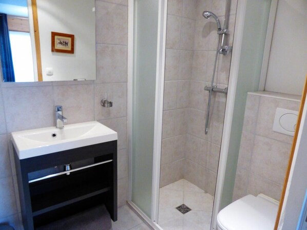 A bathroom with a white sink, dark cabinet, glass shower enclosure, and a toilet.