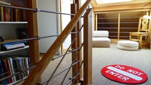 A staircase with a 'DO NOT ENTER' mat at the bottom, a bookshelf with books, and a view of a room with a bed and a chair.