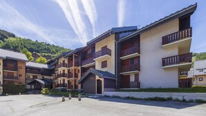 A multi-story hotel with balconies, a courtyard, and a mountainous backdrop. - 200m from shops, Ground floor, balcony, tv, ski locker, 29m², Valloire (Valloire)