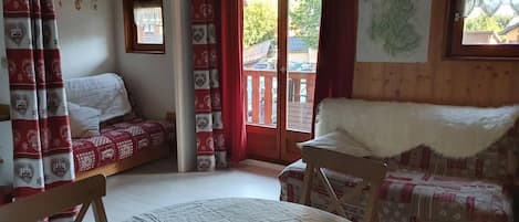 A cozy room with a bed, a sofa, and a dining table. There is a window with a view of trees and a building outside.