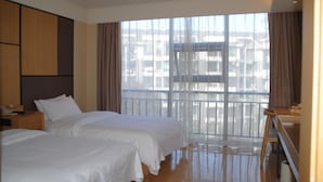 Een hotelkamer met twee bedden, een nachtkastje, een bureau en een groot raam met gordijnen.