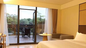 Een hotelkamer met een bed, een klein rond tafeltje, een bank en uitzicht op een terras met stoelen en een tafel.