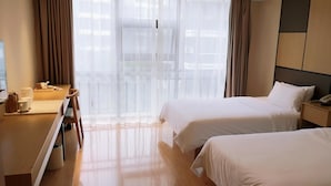Een hotelkamer met twee bedden, een bureau met stoel, een nachtkastje met telefoon, en dunne gordijnen voor het raam.