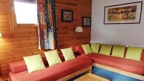 A cozy living room with a wooden floor, a red sofa with yellow cushions, a wooden coffee table, and a colorful curtain. - 26m from ski slopes, 4th floor, balcony, tv, ski locker, 35m², Valmorel (Valmorel)