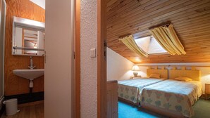 Een gezellige slaapkamer met twee bedden, een raam met gordijnen, een nachtkastje met een lamp en een houten plafond.