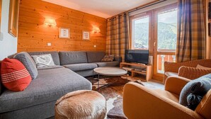 Een gezellige woonkamer met een grijze bank, een ronde salontafel en een televisie op een houten dressoir.