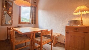 Een houten eettafel met stoelen, een spiegel, een raam met gordijnen en een lamp op een houten kast.