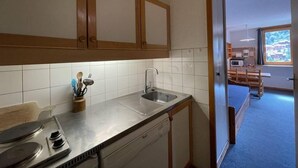 Een kleine keuken met een spoelbak, fornuis en kastjes.
