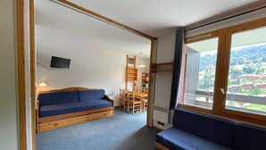 Een kamer met een blauwe bank, een houten tafel en een aan de muur bevestigde televisie.