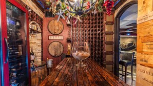 Un coin bar avec une table en bois, des bouteilles de vin et un verre à vin.