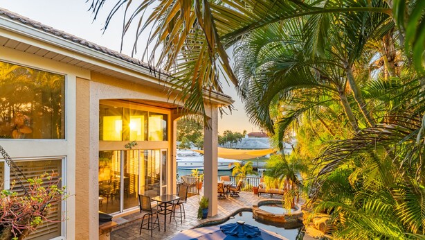 Une maison moderne dotée d’un patio aménagé avec des meubles d’extérieur, une piscine et une végétation tropicale luxuriante.