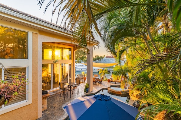 Relax in a serene outdoor space surrounded by lush plants and palm trees, complete with comfortable seating and a soothing water feature.
