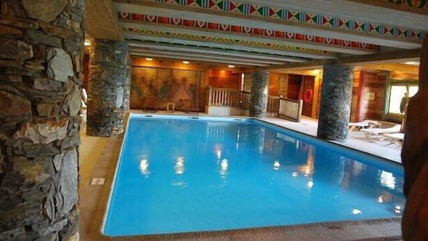 An indoor swimming pool with stone walls and colorful geometric ceiling decorations.