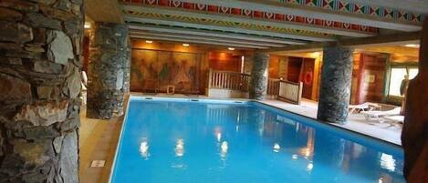 An indoor swimming pool with stone walls and colorful geometric ceiling decorations.