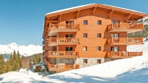 A multi-story wooden building with balconies, set against a snowy mountain backdrop.