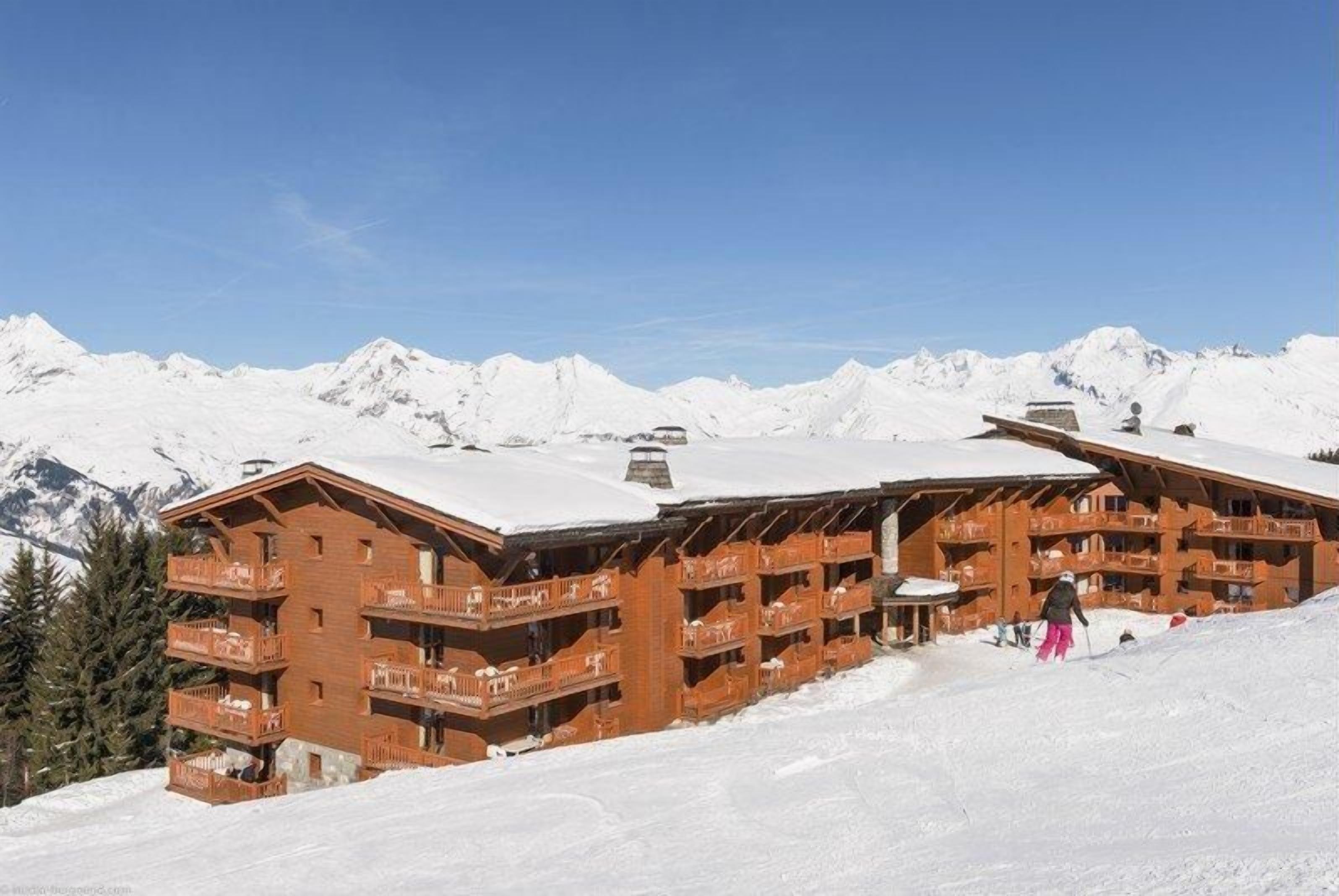 A wooden chalet with multiple balconies, set against a backdrop of snow-covered mountains.